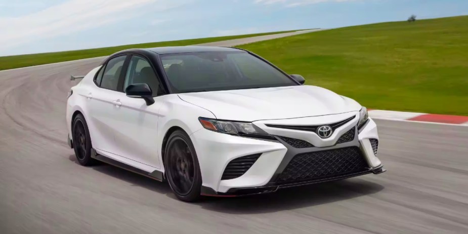 A white 2024 Toyota Camry midsize sedan is driving on a track. 