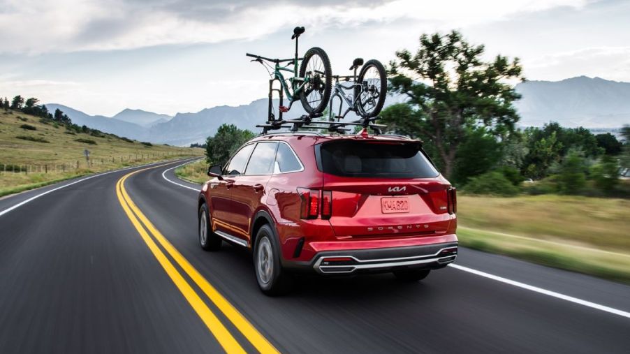 A red 2024 Kia Sorento driving down the road with bikes on the roof.
