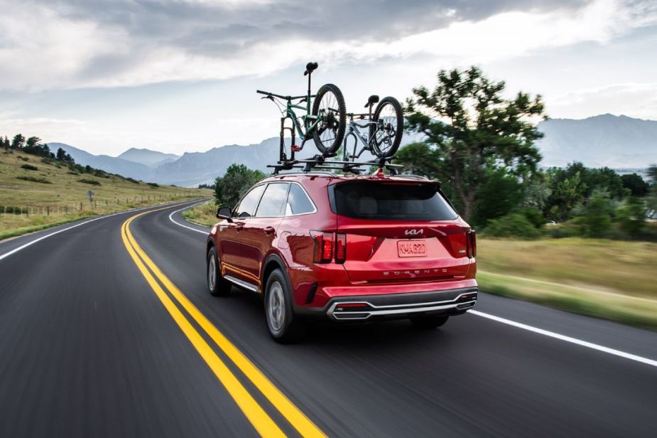 A red 2024 Kia Sorento driving down the road with bikes on the roof.