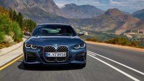 The front grille of a blue 2024 BMW 4 Series driving with mountains in the back. This is the most dependable luxury car of 2023.