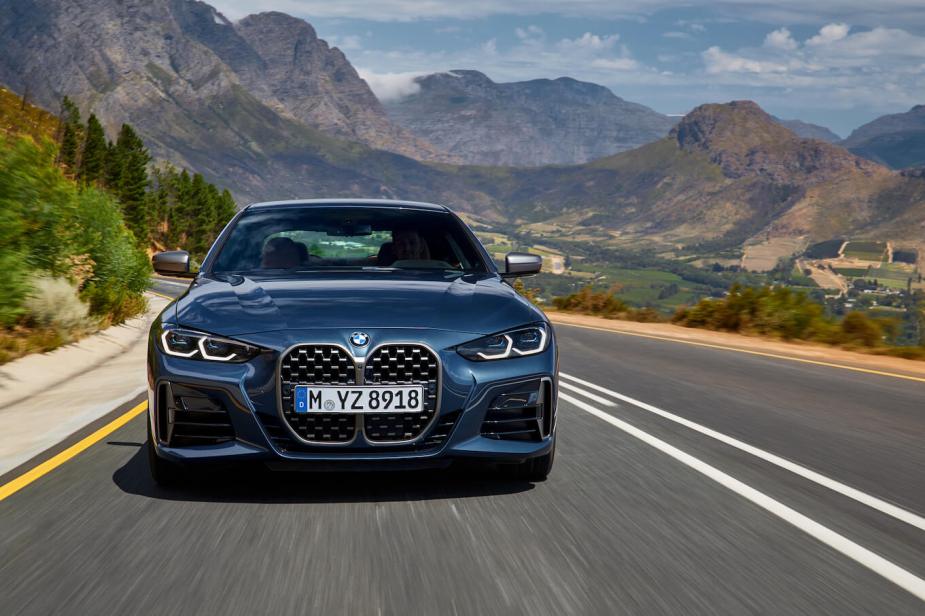 The front grille of a blue 2024 BMW 4 Series driving with mountains in the back. This is the most dependable luxury car of 2023.