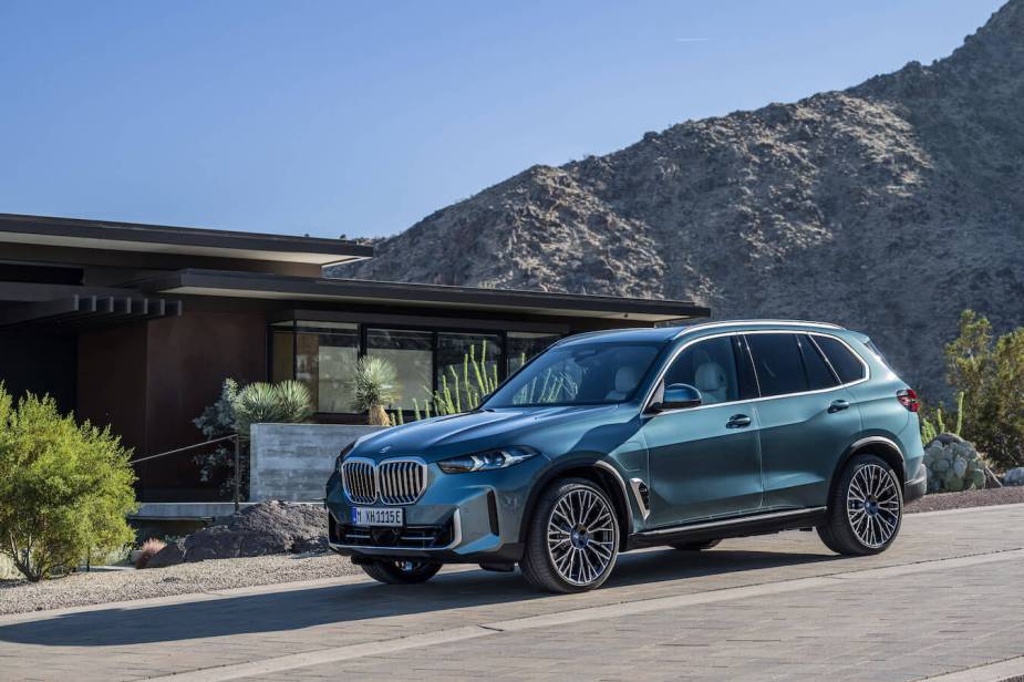 A blue BMW X5 driving down a hill with mountains behind. The X5 and 8 Series are holding back BMW sales this year.
