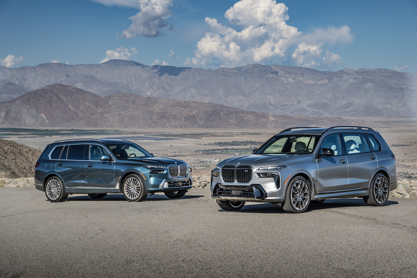 Two BMW X7 models parked in the desert in front of some mountains.