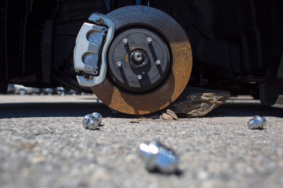Vehicle's brake rotor rests on the ground, lug nuts on the pavement nearby.