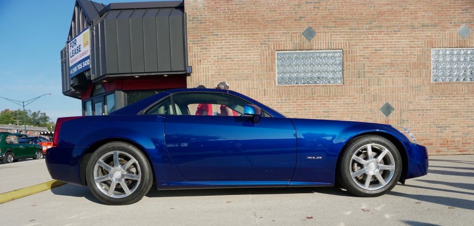 Blue Cadillac XLR coupe parked in front of a brick wall.