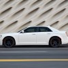 A white Chrysler 300 shows off its classic American car lines while it drives on a city street.