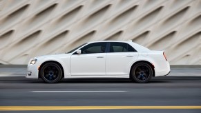 A white Chrysler 300 shows off its classic American car lines while it drives on a city street.
