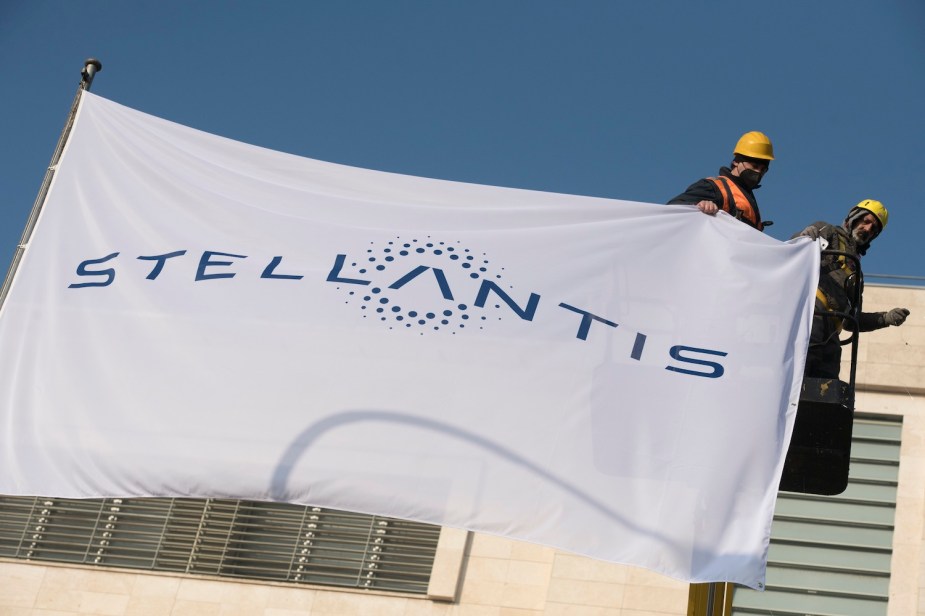 Workers hoist a Stellantis logo flag above a former Chrysler Corporation office.