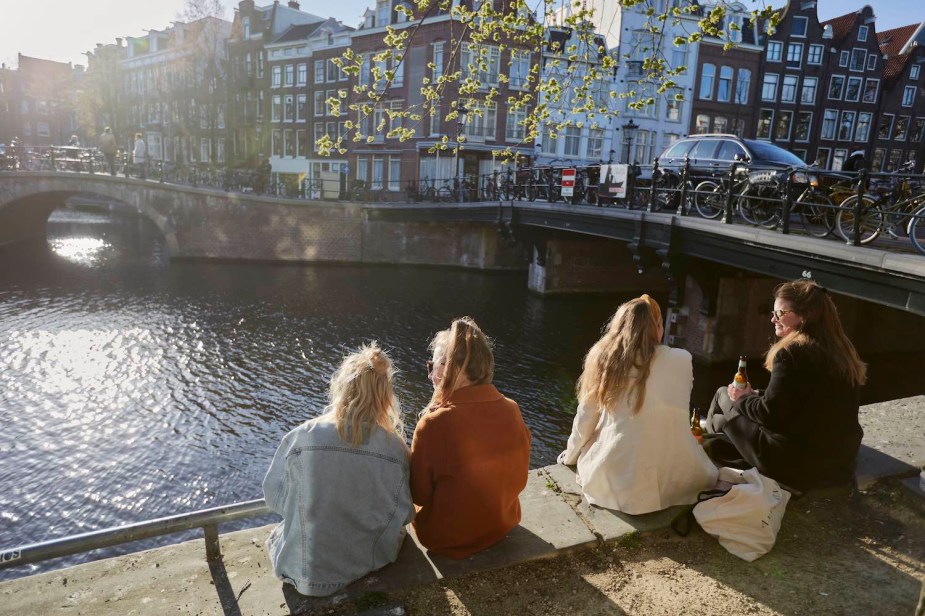 Four women sit on the edge of a canal overlooking Amsterdam in the Netherlands.