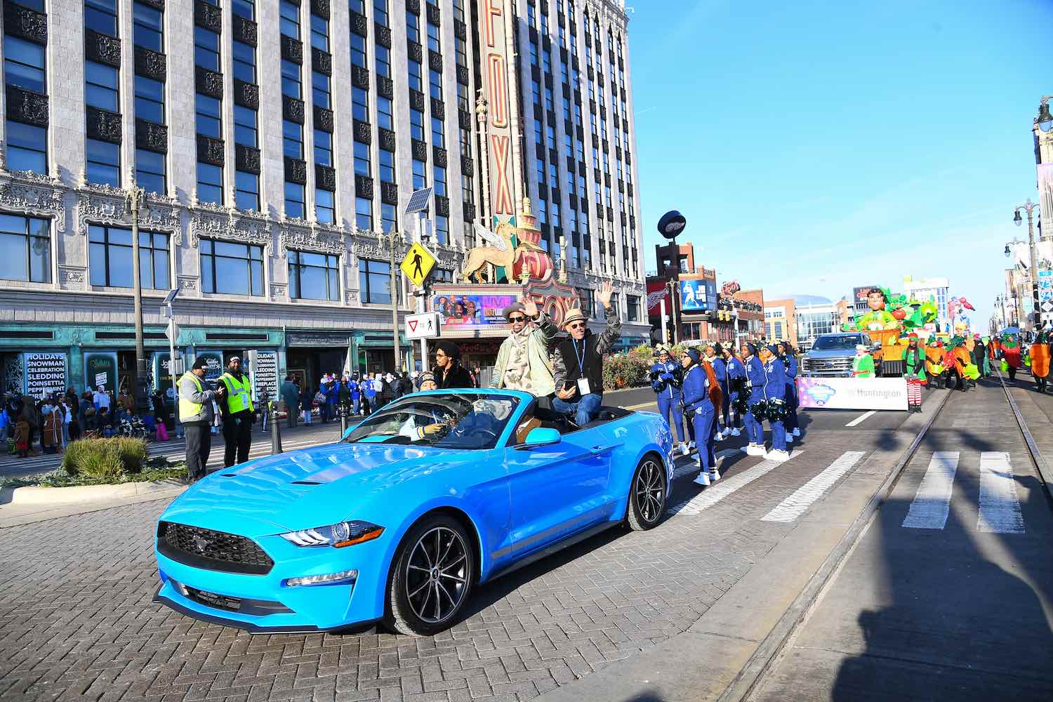 A bright blue Mustang leads a thanksgiving parade down Detroit Michigan's Woodward Avenue.