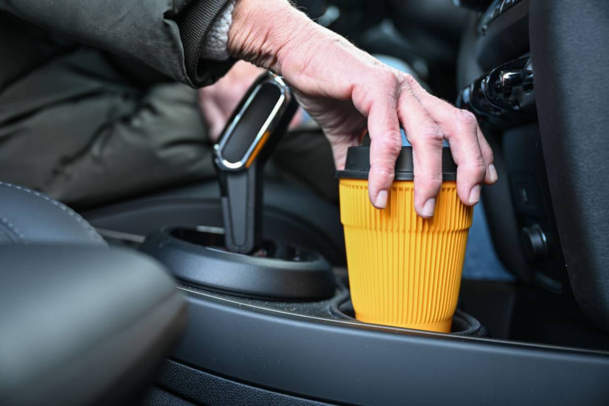 A person with a cup of coffee in their car to drink.