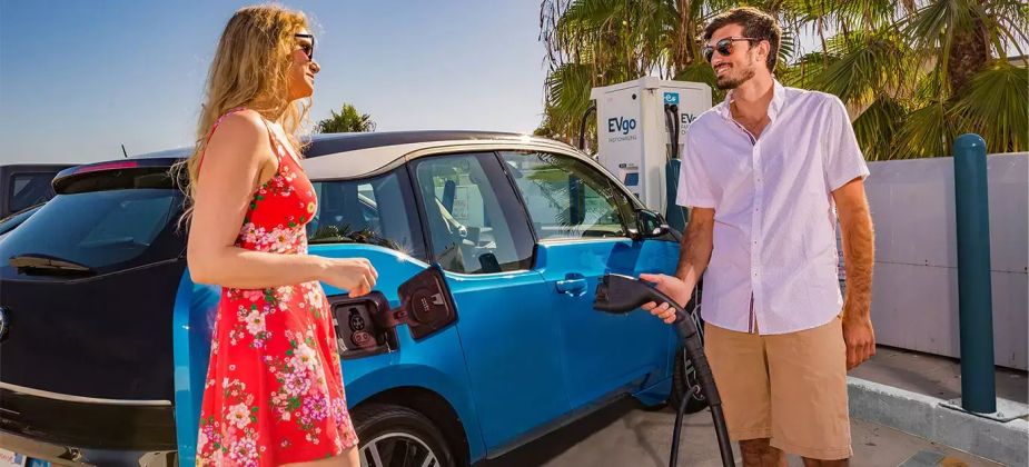 A man and woman plug their blue EV into a DC fast charger built and installed by EVgo.