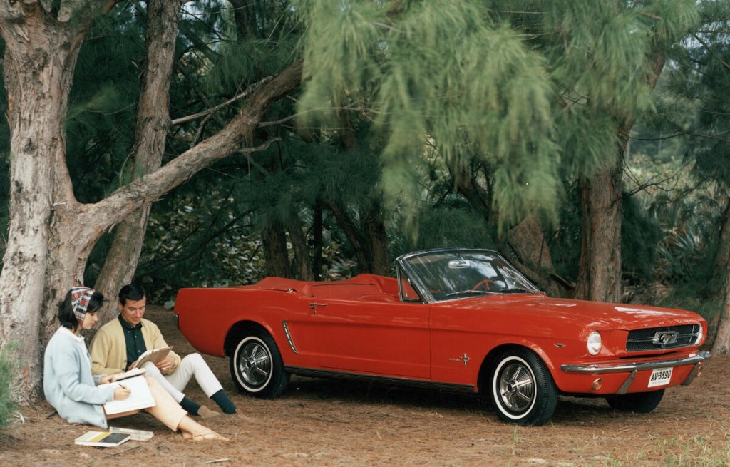 Red 1964 1/2 Ford Mustang convertible under tree