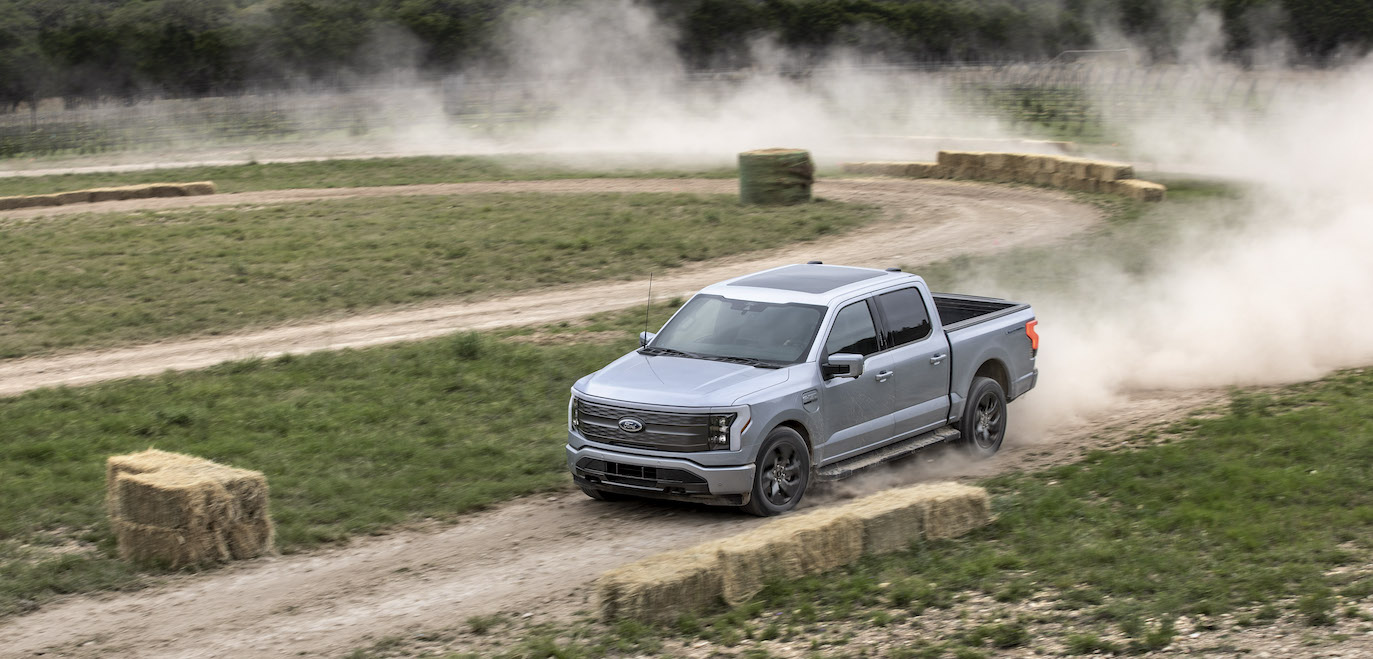 A silver Ford F-150 Lightning Lariat driving on a dirt road. The F-150 Lightning's price is an advantage over the Rivian R1T