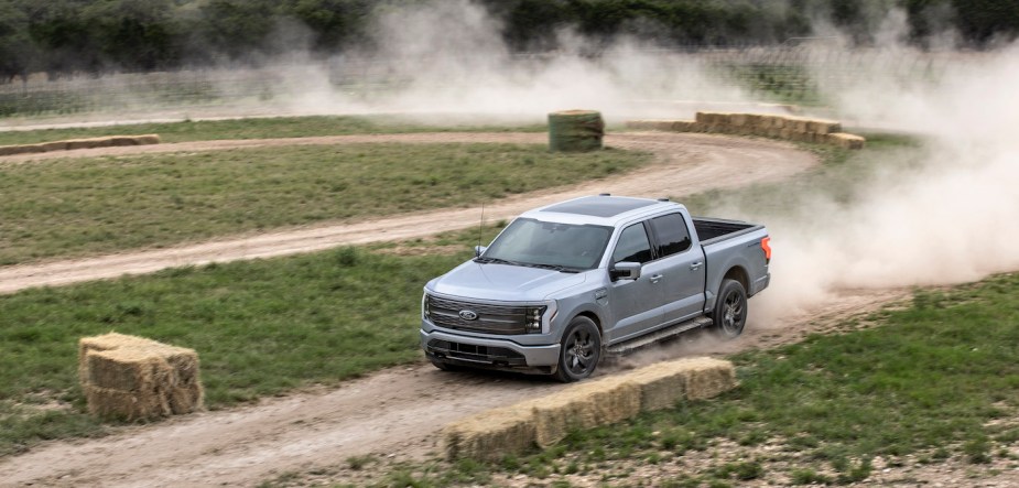 A silver Ford F-150 Lightning Lariat driving on a dirt road. The F-150 Lightning's price is an advantage over the Rivian R1T