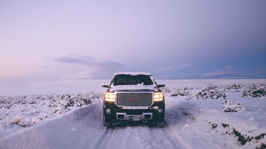 Black GMC Sierra 1500 pickup truck drives down a snowy road.