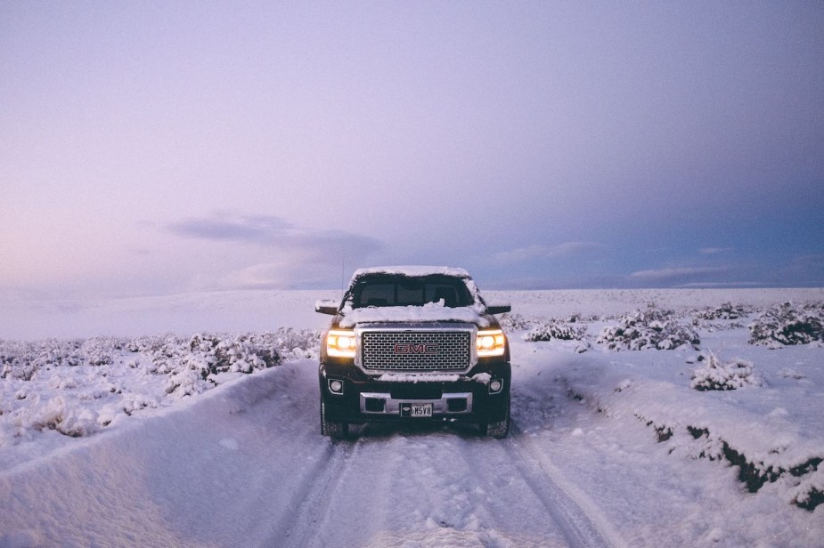 A black GMC Sierra 1500 pickup truck drives down a snow-covered road.
