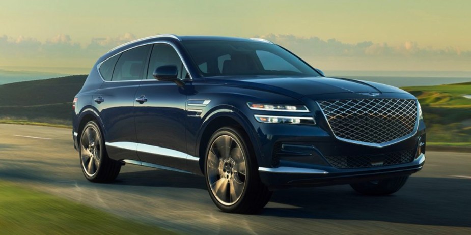A blue Genesis GV80 midsize luxury SUV is driving on the road. 