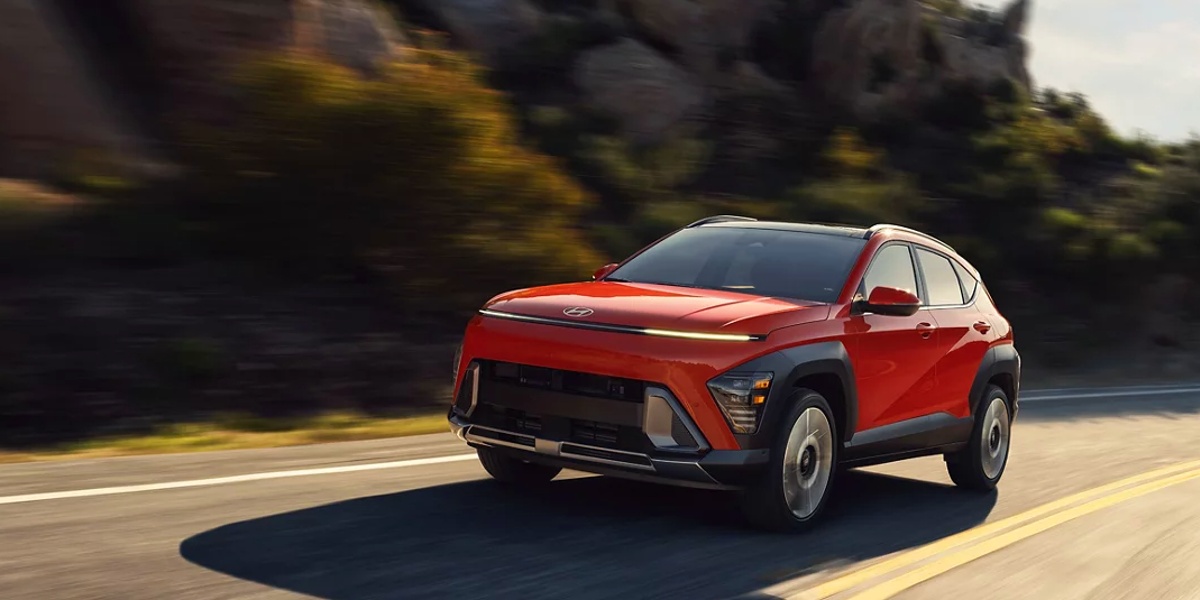 An orange 2024 Hyundai Kona subcompact SUV is driving on the road.