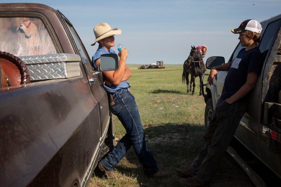 Cattle ranchers lean against their traditional, ICE pickup trucks.