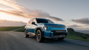 A blue Kia EV9 electric SUV driving while the sun sets behind it.