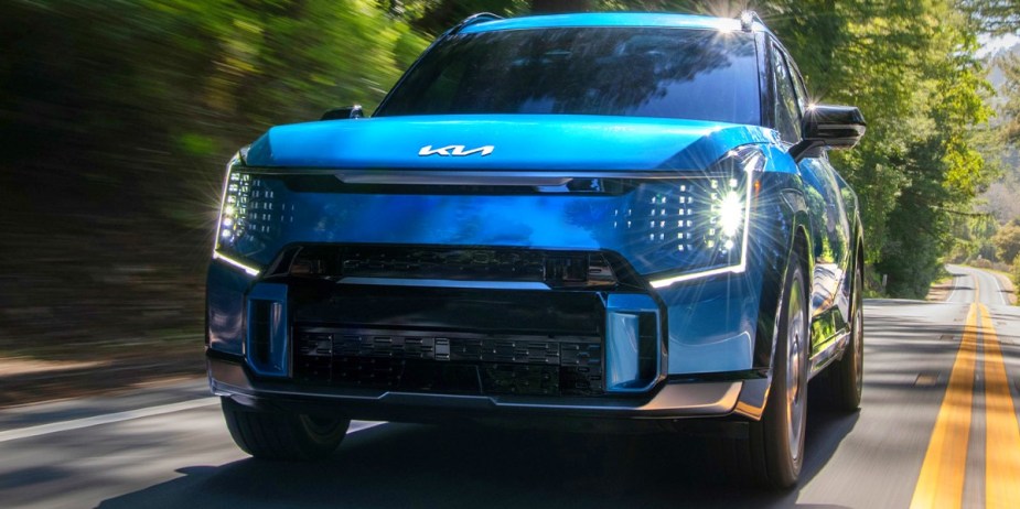 A blue 2024 Kia EV9 midsize three-row electric SUV is driving on the road. 