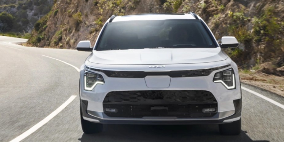A white Kia Niro EV subcompact electric SUV is driving on the road. 