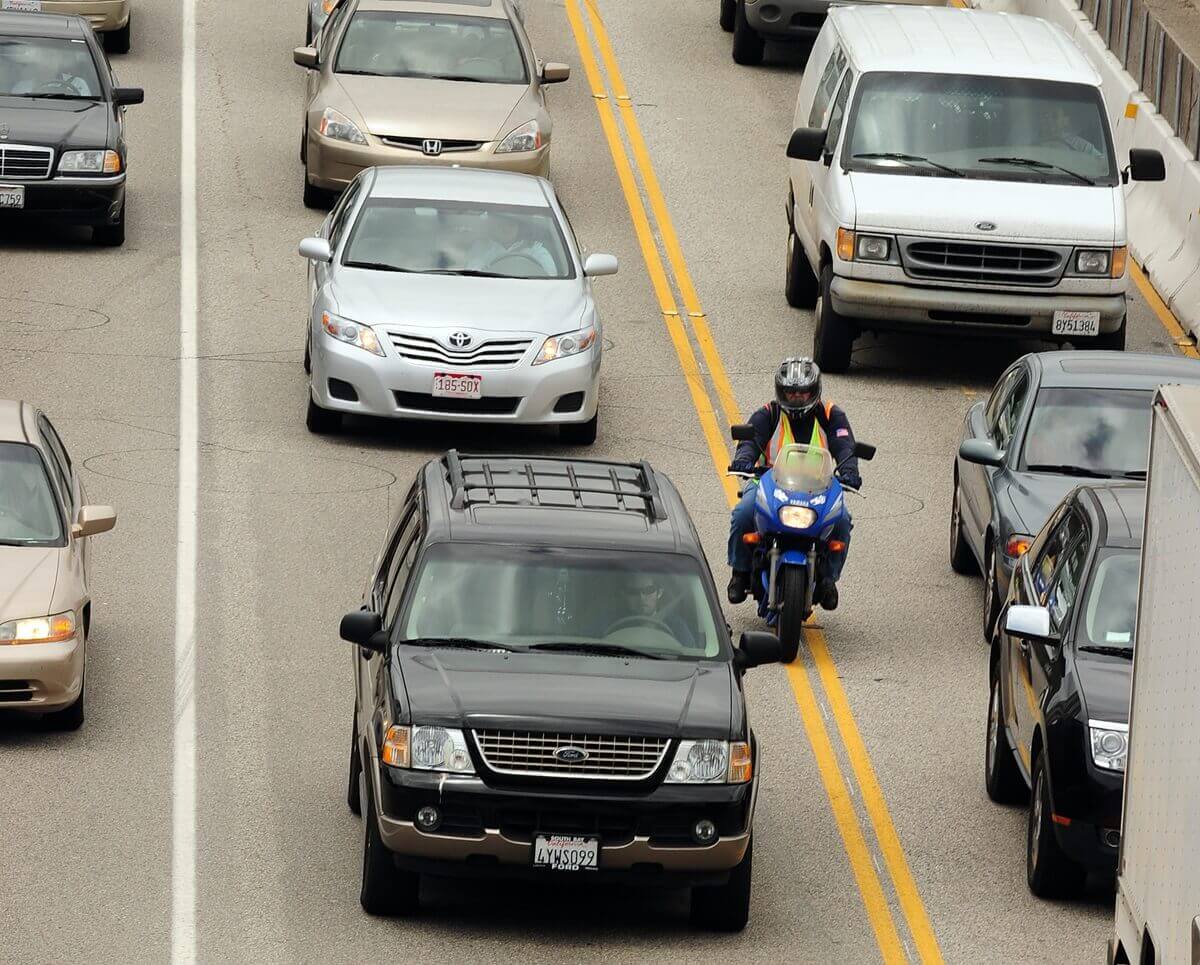 A motorcycle rider in safety gear engages in lane splitting on a California highway.