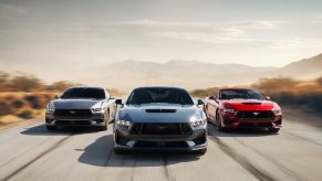 A set of 2024 Ford Mustang EcoBoost and GT Convertibles and Coupes drive on an open road.