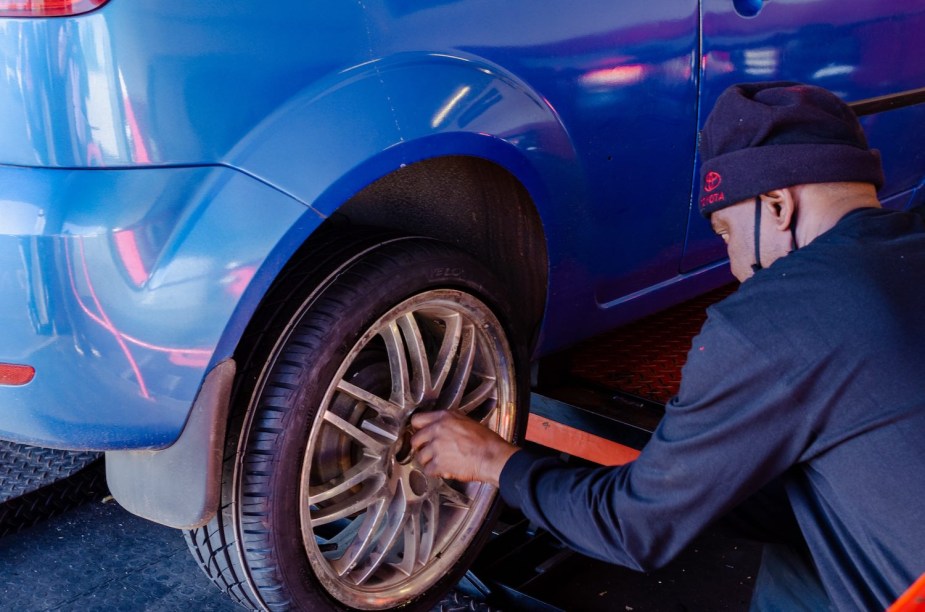 A man struggles with stuck lug nuts while changing the tire of a car.