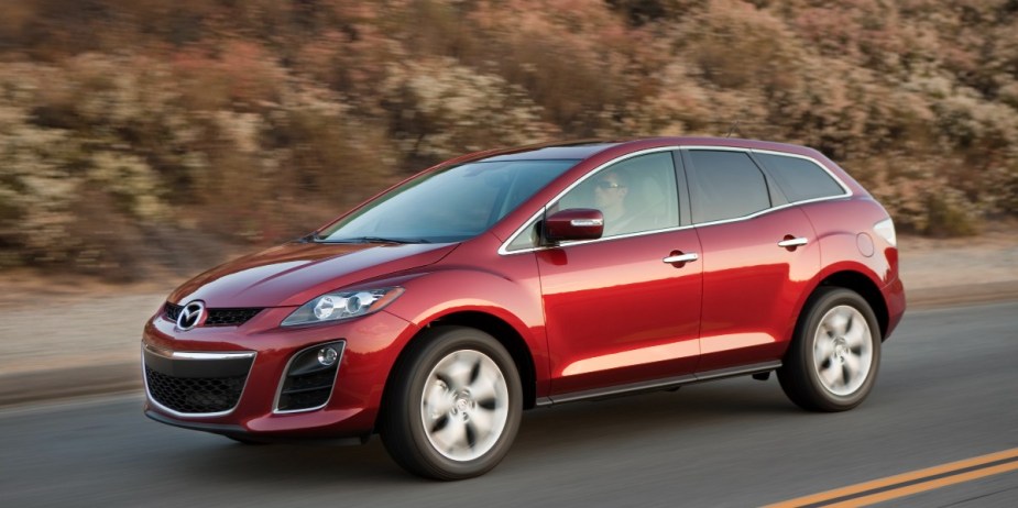 A red Mazda CX-7 midsize SUV is driving on the road. 
