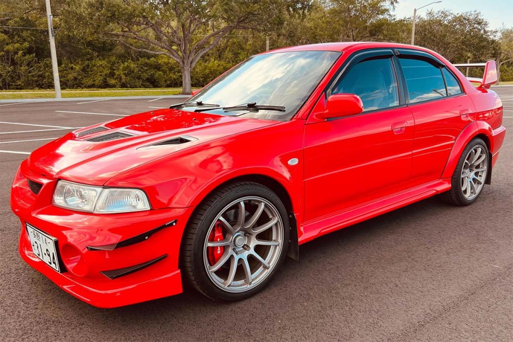 Bright red Mitsubishi Lancer Evolution IV front 3/4 sold on Cars and bids with Low Mileage sitting on the street in front of trees