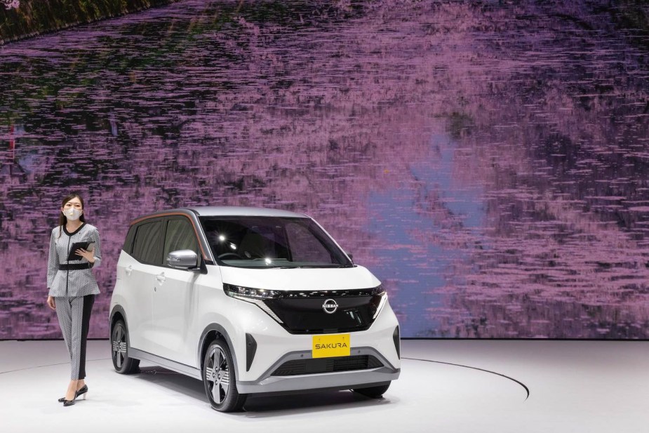 A woman stands on stage to present the new Nissan Sakura KEI Class EV crossover car.