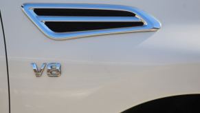 The chrome V8 badge on the fender of a white Nissan Titan pickup truck.
