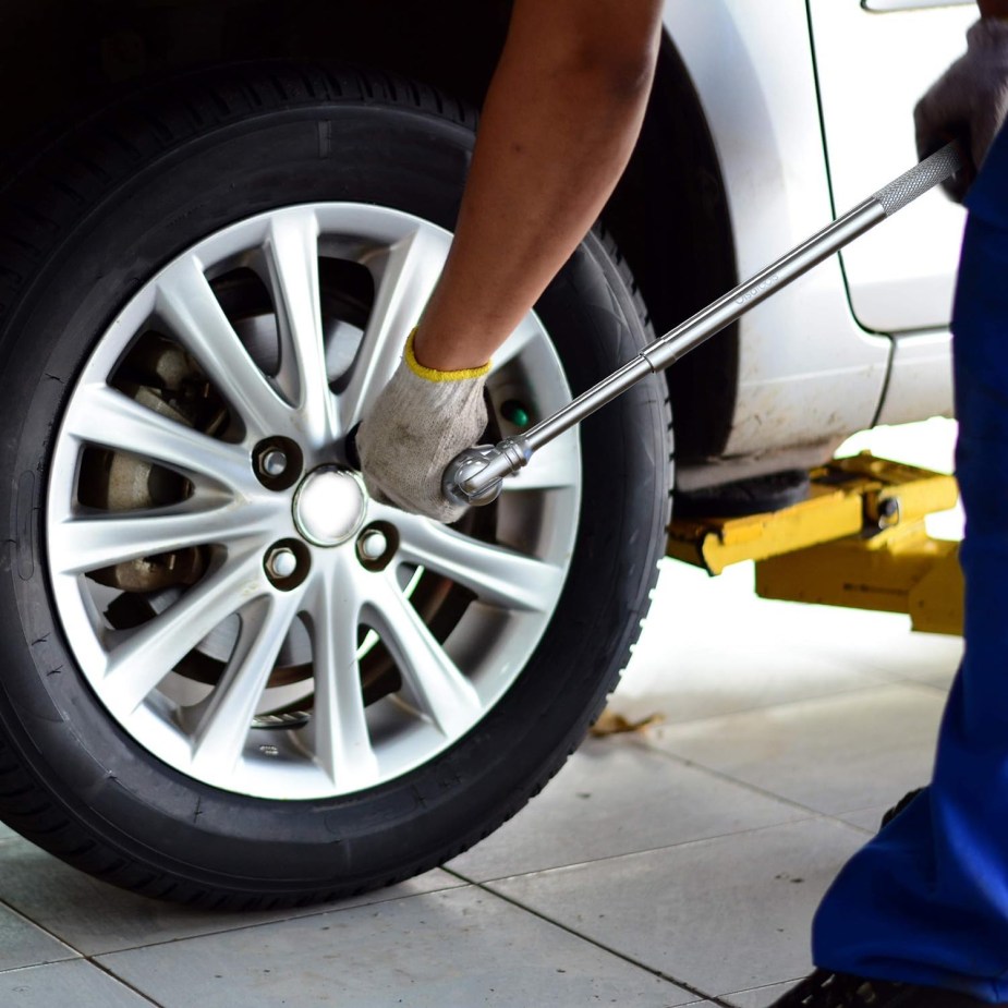 A mechanic's hands use a breaker bar to free up stuck, rusty lug nuts during a tire change.
