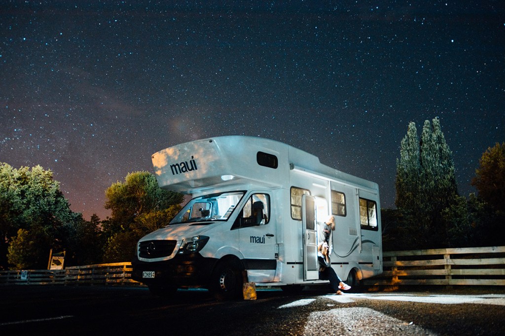A camper van / RV parked at a campground at night with stars in the background