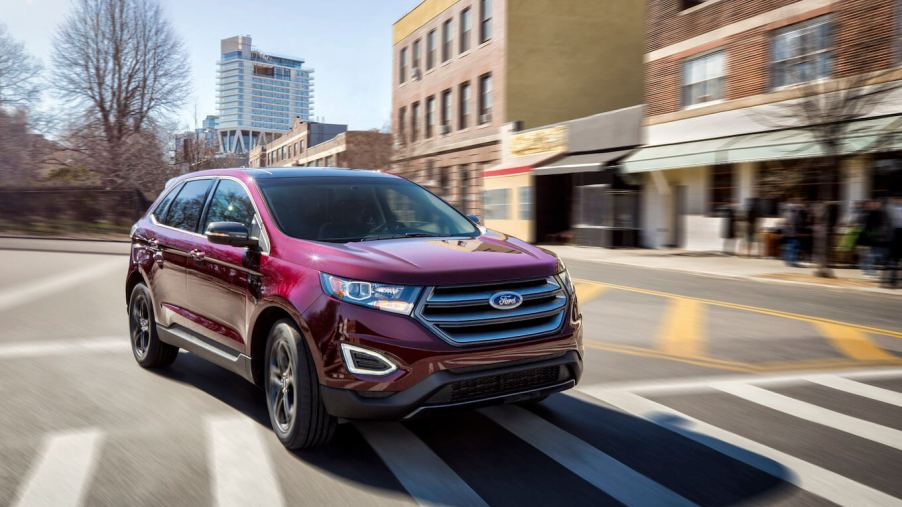 A red 2018 Ford Edge driving on a city street. This is one of the reliable Ford Edge models.