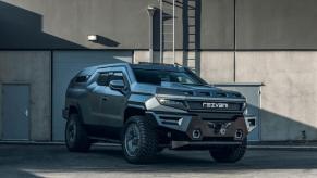 A 2023 Rezvani Vengeance full-size off-road SUV model parked in front of a gray building, garage door, and ladder