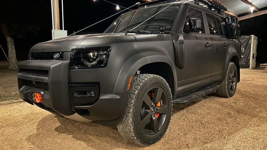 A matte black Land Rover Defender 130 sits under a pavilion at the TReK 2023 event in Texas.