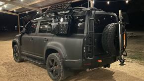 A matte black Land Rover Defender 130 shows off its shovel, spare tire, and high-lift jack.
