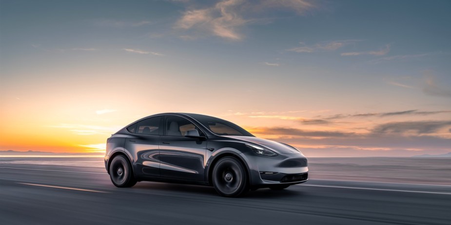A black Tesla Model Y small electric SUV is driving on the road. 