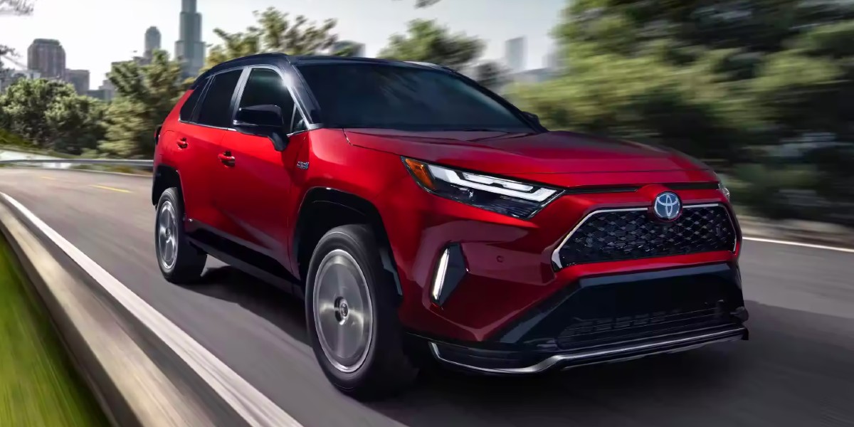 A red 2024 Toyota RAV4 Prime small plug-in hybrid SUV is driving on the road.