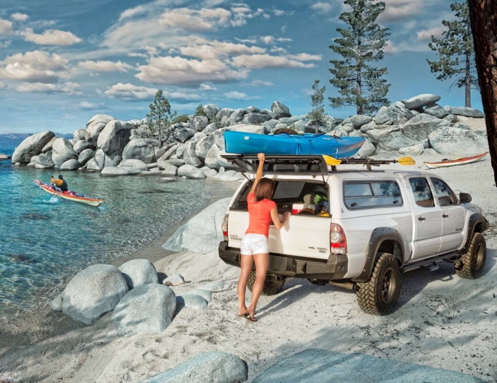 A woman pulls a boat from the roof of a Toyota Tacoma with a camper shell pickup truck cap.