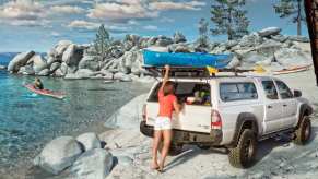 A woman pulls a boat from the roof of a Toyota Tacoma with a camper shell pickup truck cap.