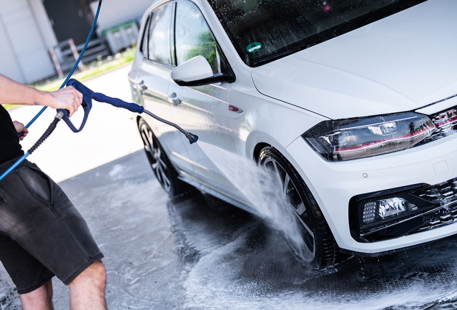 A white Volkswagen Polo GTI being sprayed with a pressure washer and soap at a car wash