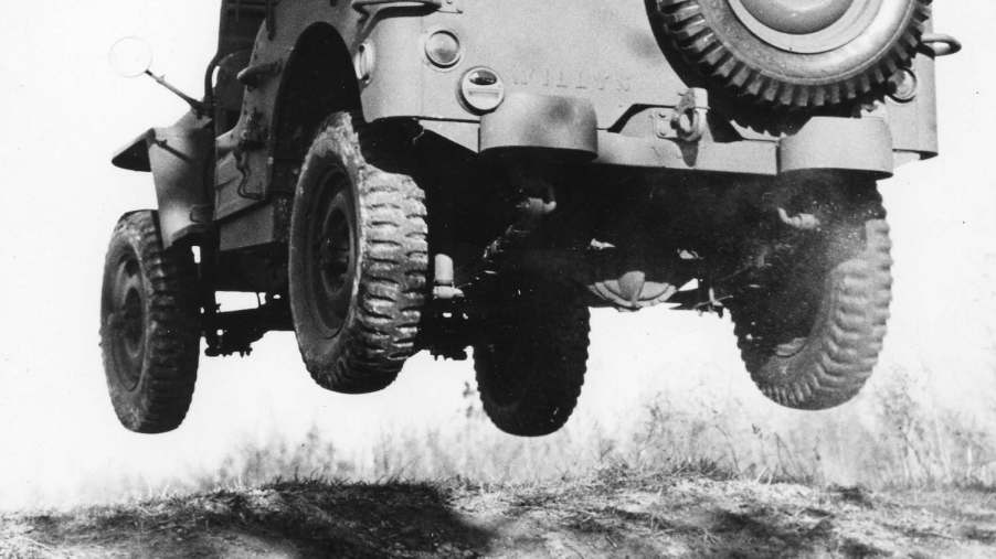 Black and white photo of a man in a fedora completing a jump across sand dunes in a Willys-Overland military GP Jeep prototype.