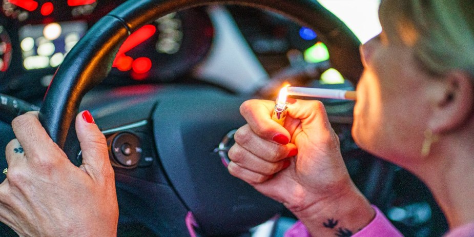  A woman lights a cigarette behind the wheel of her car.