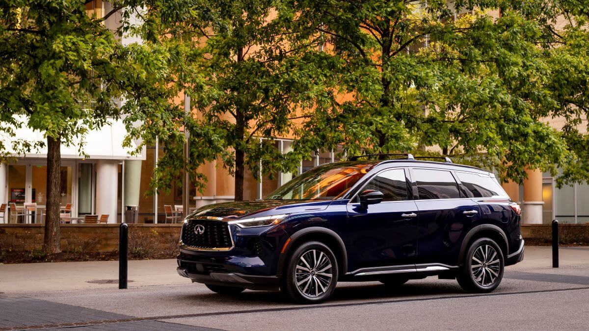 A 2024 Infiniti QX60 midsize luxury crossover XUV model parked in a plaza near trees and bollards