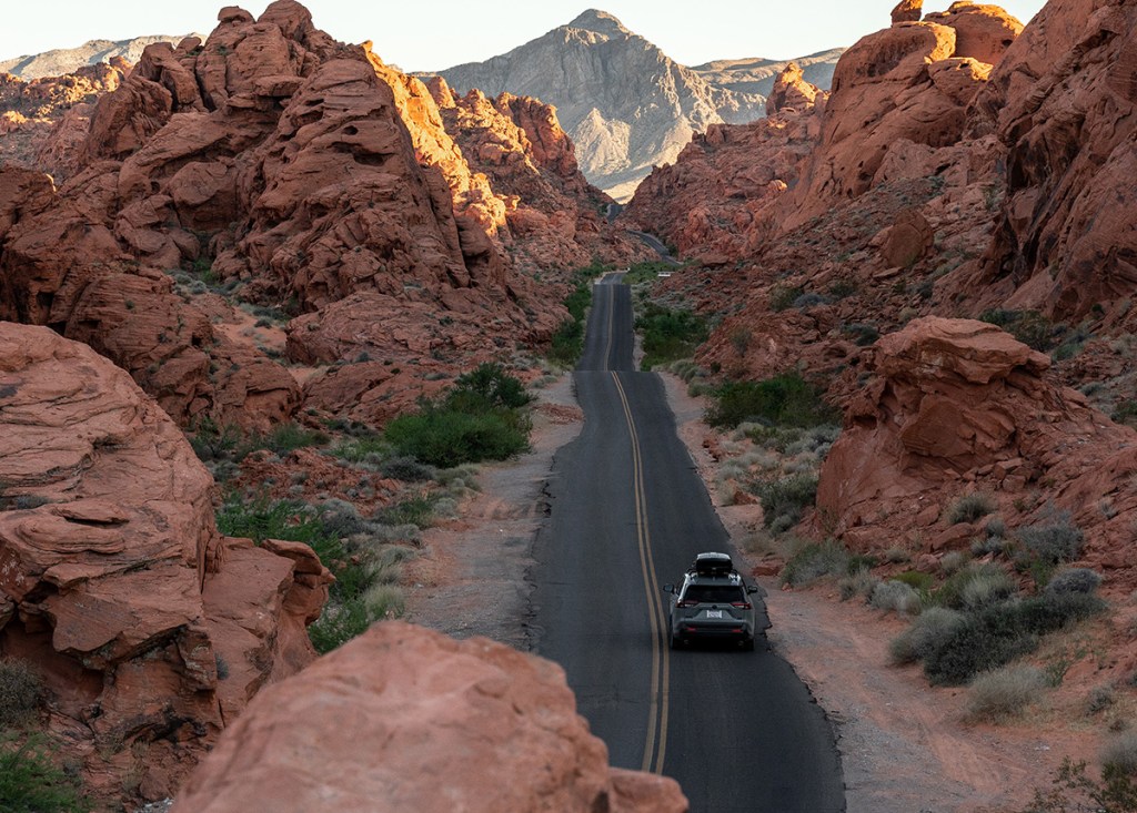A car with a roof box driving through Moab Utah natural rock formations on a road trip