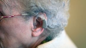 A woman with gray hair and glasses wearing an auditive hearing aid prosthesis on her left ear